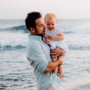 man holding daughter on the beach in blue shirt | Island Real Estate